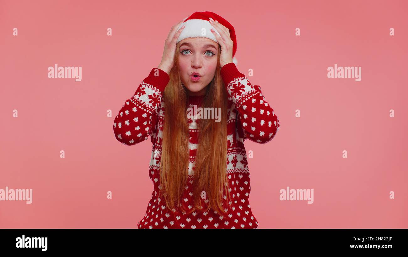 Teen erwachsenen Mädchen in Weihnachtshut Heben Hände in Überraschung schockiert durch plötzlichen Sieg, wow Emotion Stockfoto