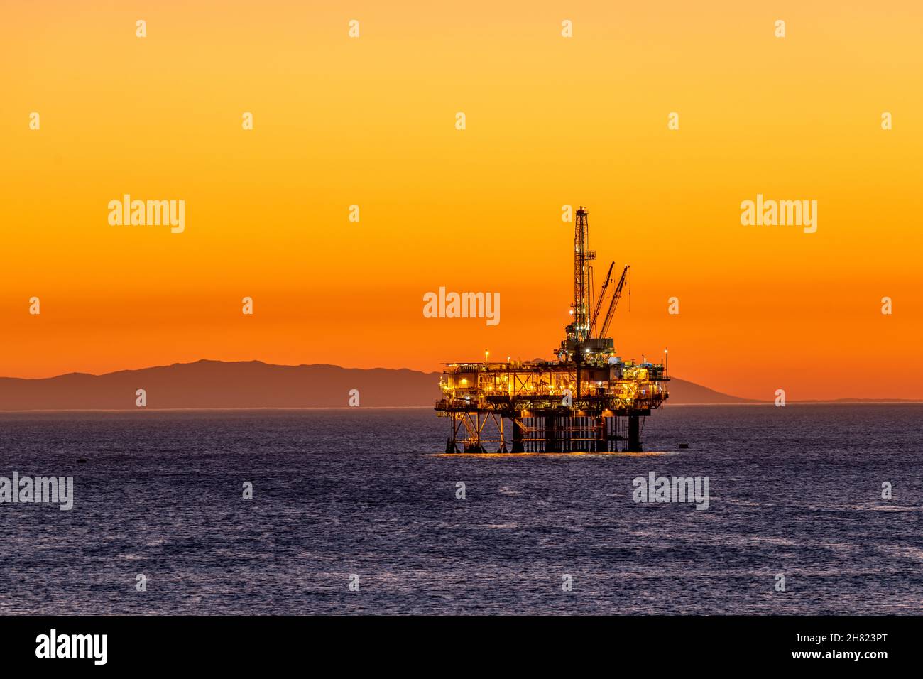 Offshore-Ölplattform vor der Küste Kaliforniens gegen einen launischen, orangen Himmel, wenn die Sonne hinter der Bohrinsel untergeht. Stockfoto