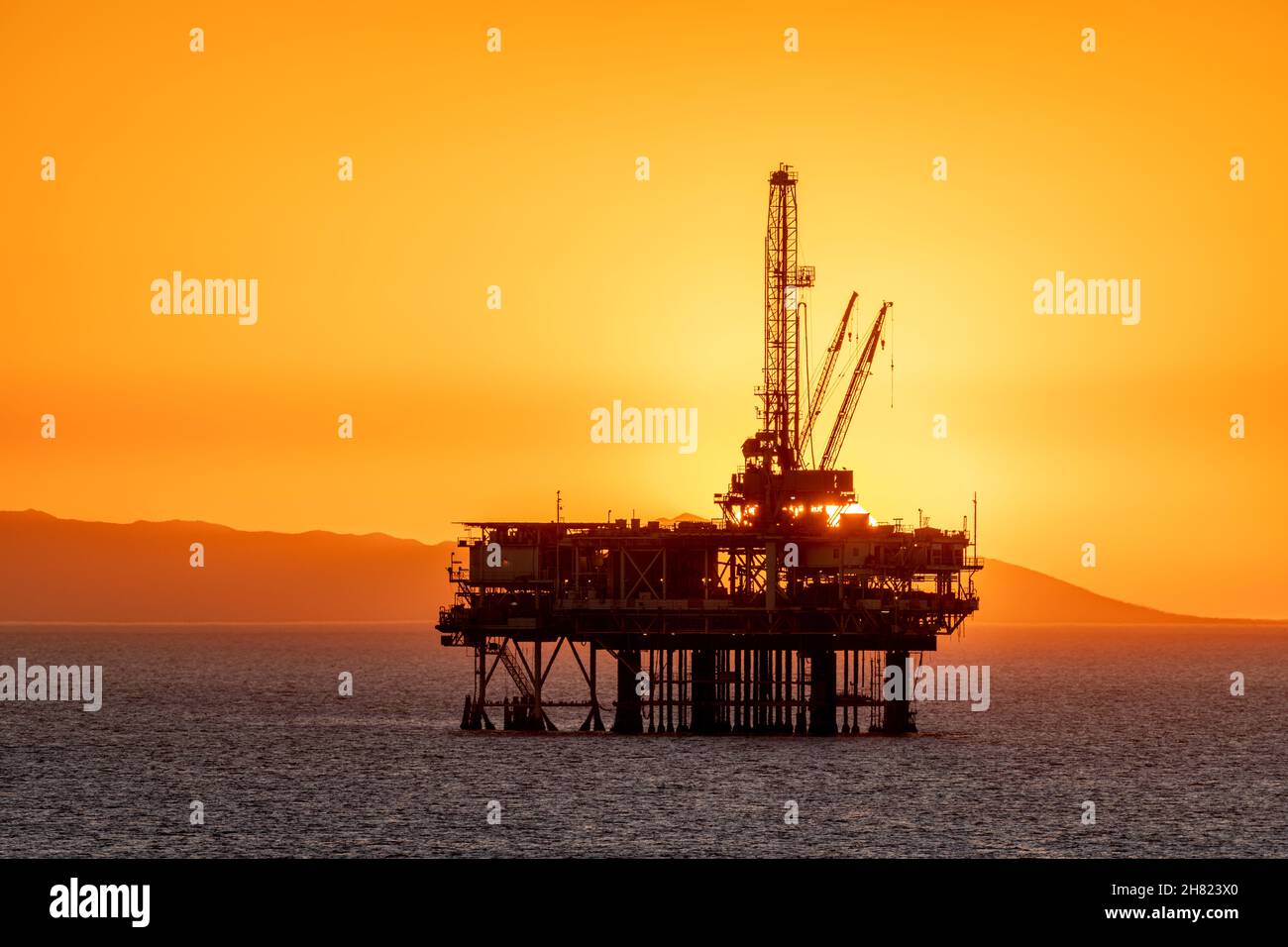 Offshore-Ölplattform vor der Küste Kaliforniens gegen einen launischen, orangen Himmel, wenn die Sonne hinter der Bohrinsel untergeht. Stockfoto