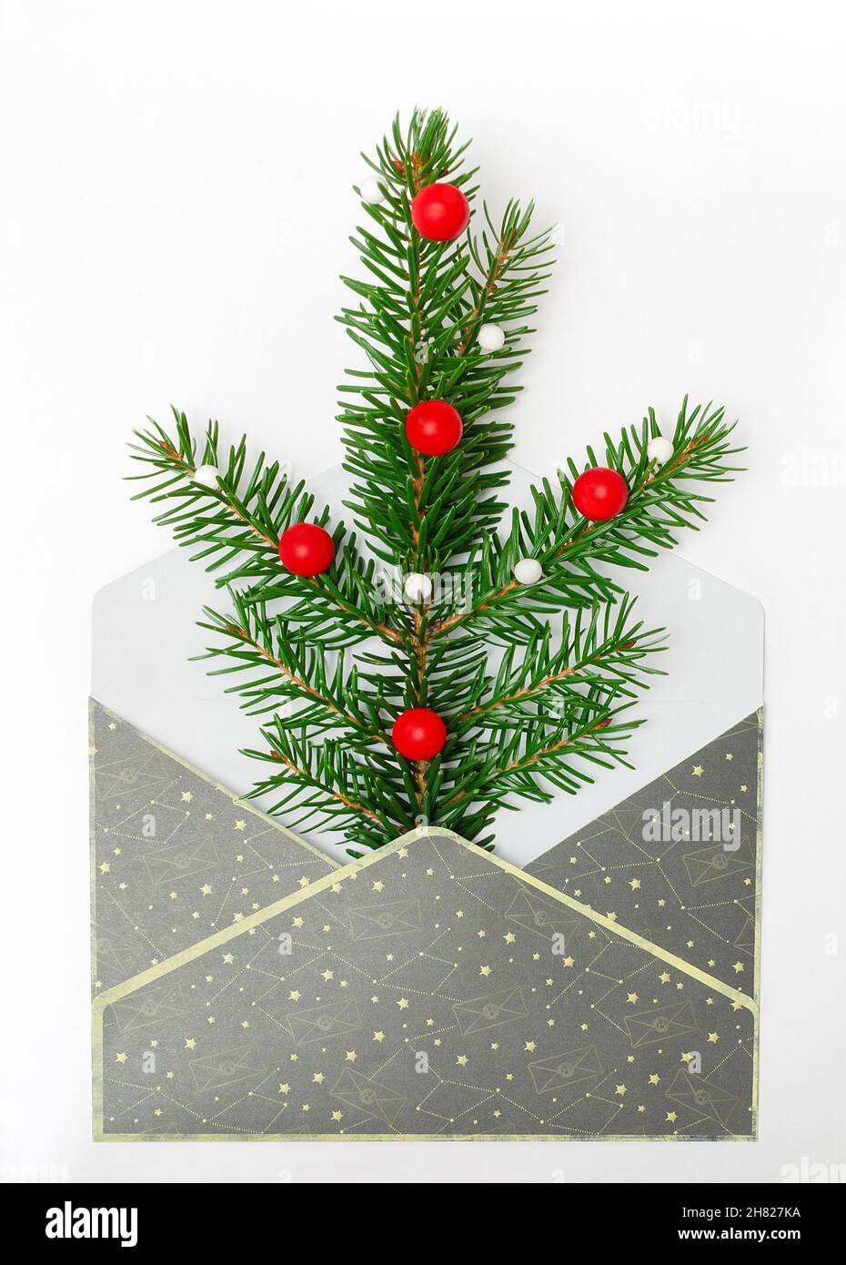 Weihnachtszweig aus Tanne in einem grauen Umschlag, Neujahrskarte. Fichtenzweig mit roten Kugeln auf weißem Hintergrund. Feiertage, Weihnachtskonzept, Stockfoto