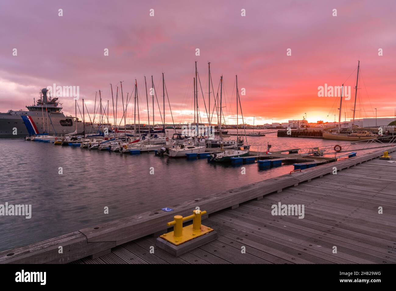 Dramatischer, farbenfroher Himmel über einem Hafen mit Segelbooten, die bei Sonnenuntergang an den Anlegestegen festgemacht sind Stockfoto