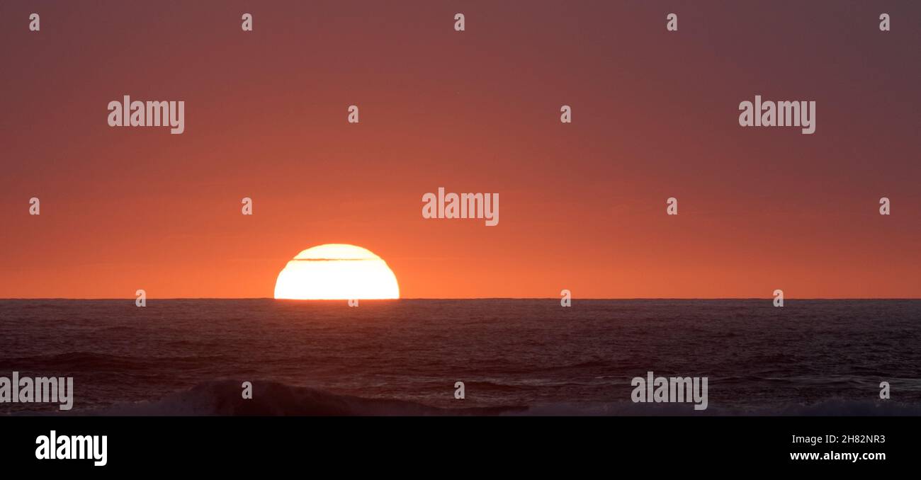 Strahlend roter Sonnenuntergang mit Sonne, die unter einen klaren Horizont taucht Stockfoto