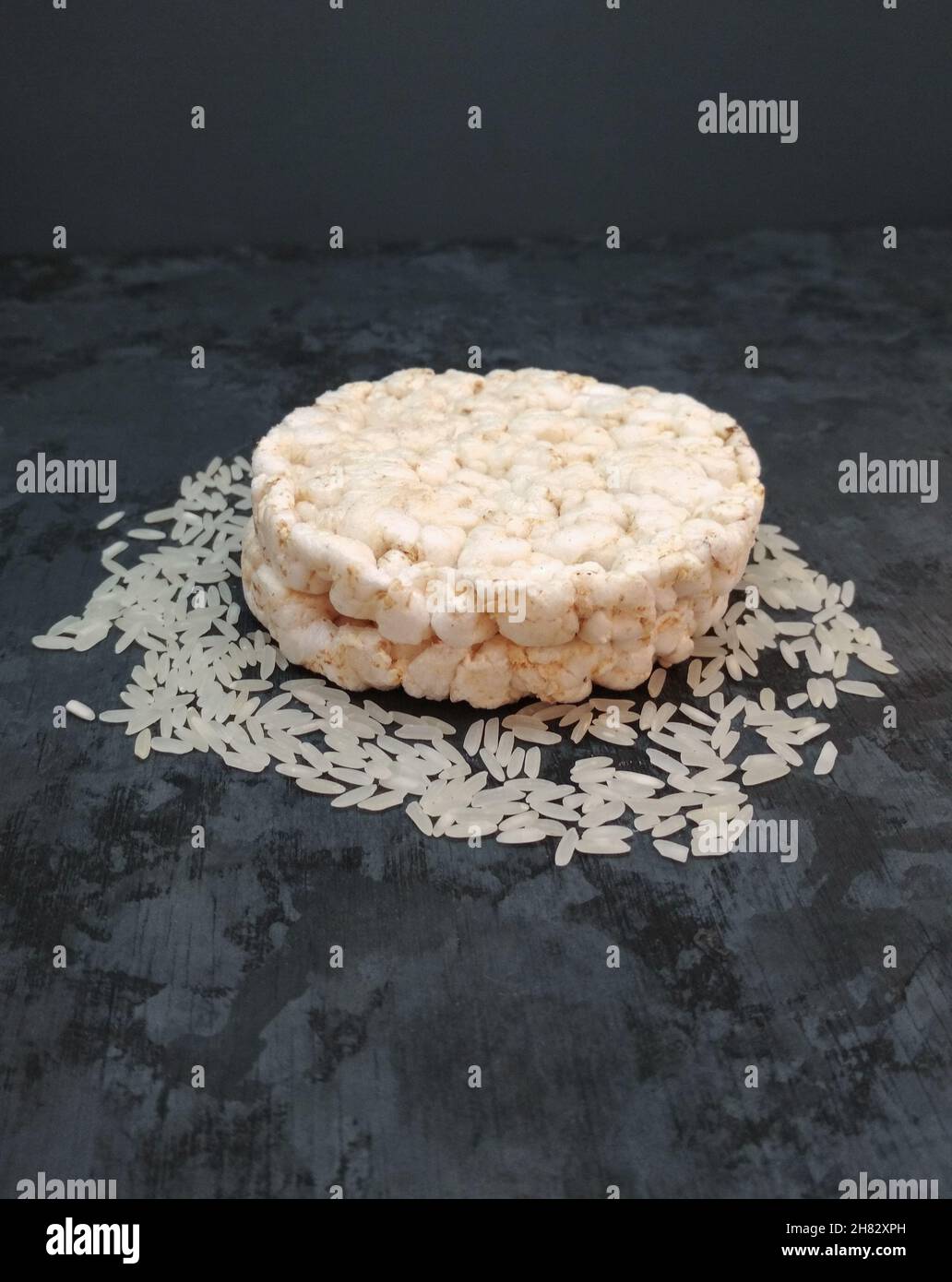 Puffreiskuchen auf ungekochten Reiskörnern isoliert auf rustikalem grauen Hintergrund Stockfoto