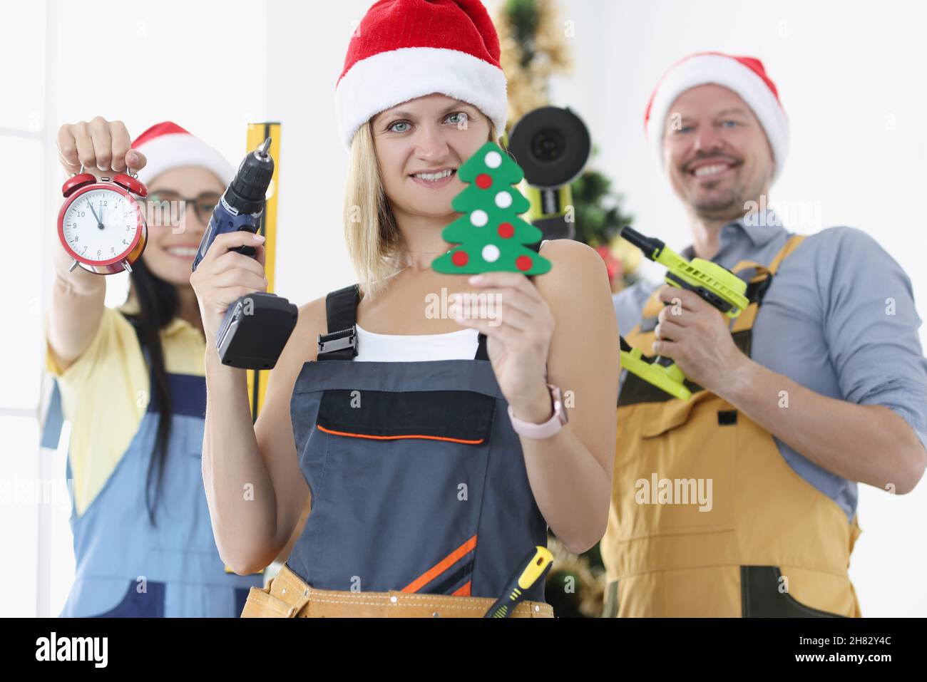 Team von Bauherren mit Arbeitswerkzeug Wecker auf dem Hintergrund von Weihnachtsbaum. Stockfoto