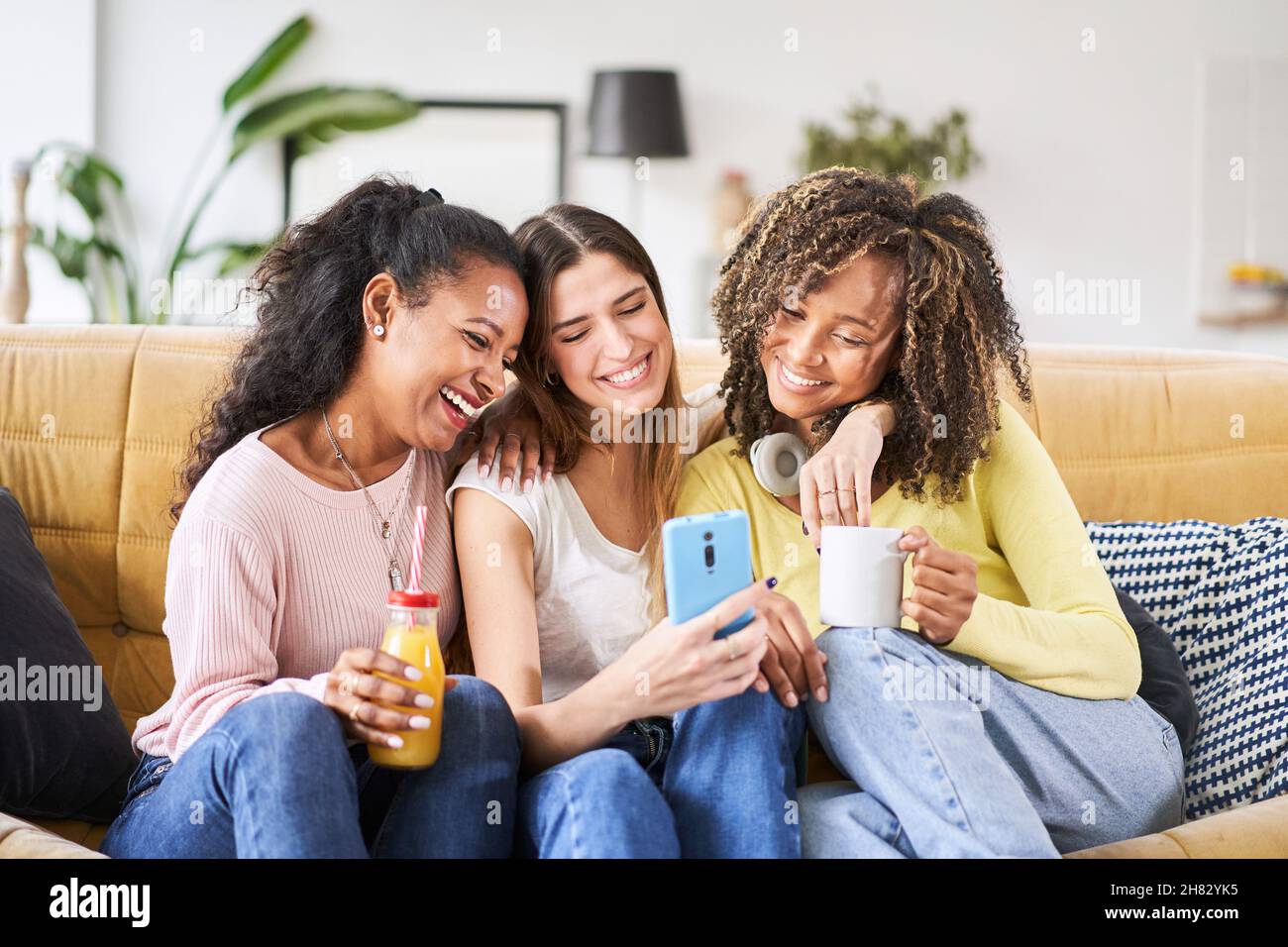 Interracial Gruppe von drei schönen jungen Freundinnen zu Hause lachen mit einem Smartphone für soziale Medien Stockfoto