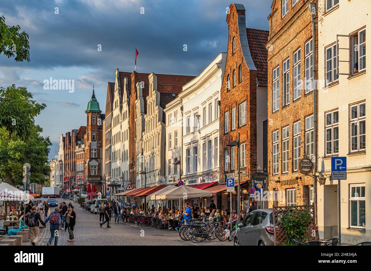Touristen schlendern am Lübecker Ufer entlang, Häuser mit traditionellen Fassaden, die vom Licht des Sonnenuntergangs erleuchtet sind. Lübeck, Deutschland, Europa Stockfoto