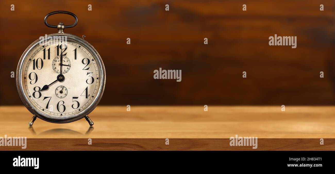 Nahaufnahme eines alten Weckers auf einem Holztisch und Hintergrund mit Kopierraum und Reflexionen. Acht Uhr, Italien. Stockfoto