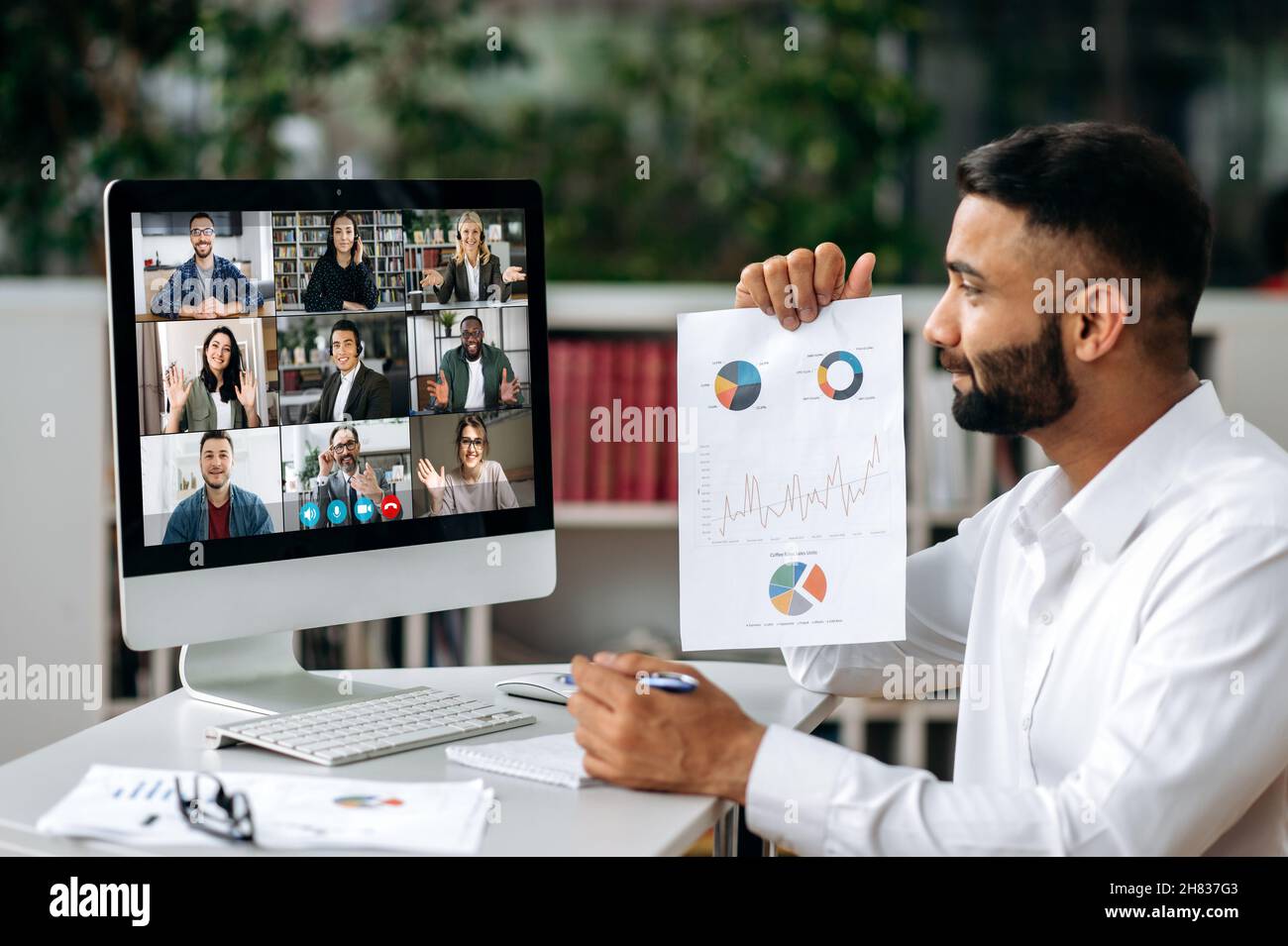 Videokonferenz, Online-Meeting. Ein intelligenter indischer Geschäftsmann oder Mentor sitzt am Arbeitsplatz, kommuniziert per Videoanruf mit seinen Partnern, diskutiert eine Strategie, zeigt eine Finanzgrafik Stockfoto