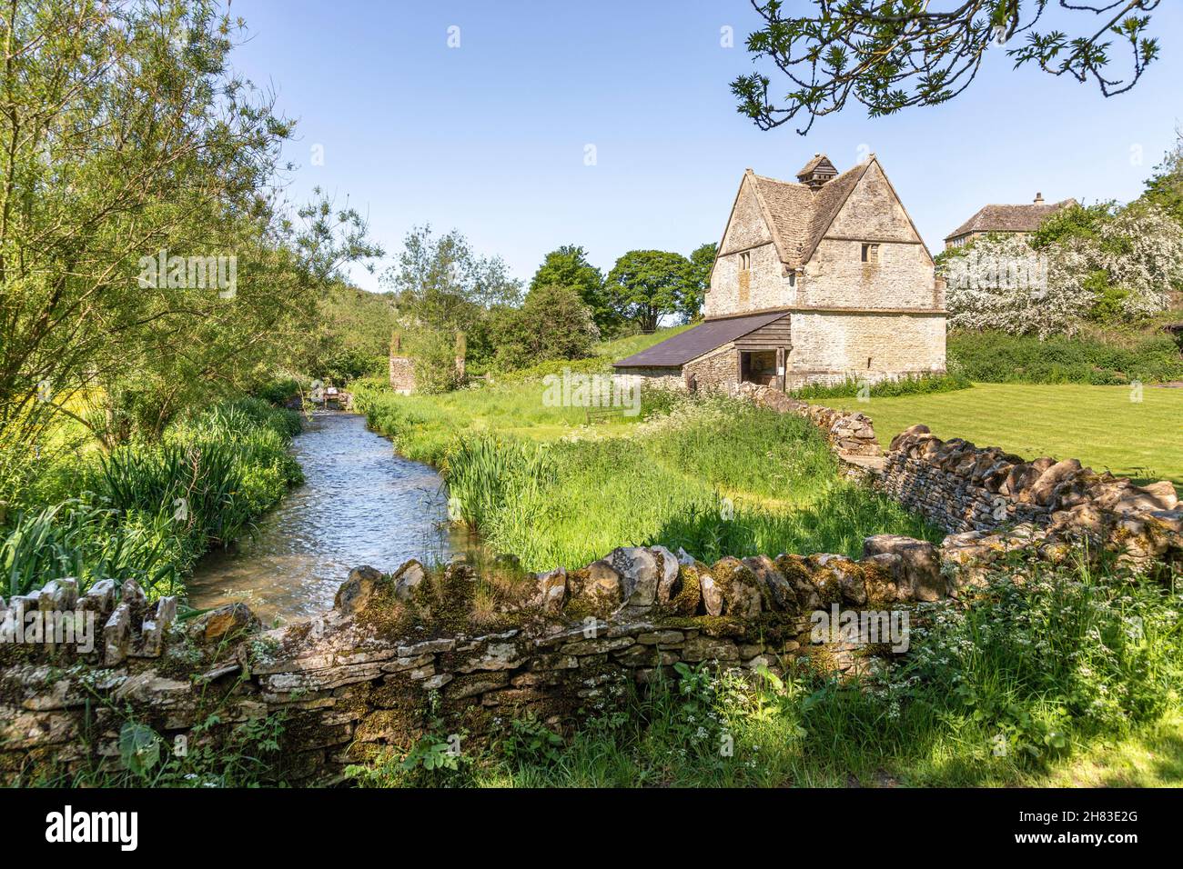 Der alte Steindovecote (um 1600 n. Chr.) neben dem kleinen Fluss Windrush, der durch das Cotswold-Dorf Naunton, Gloucestershire, Großbritannien, fließt Stockfoto