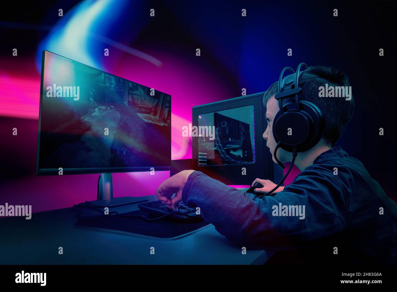 Junge Spieler spielen Spiel auf Gaming-Computer. Rosa und blaue LED-Lichter im Hintergrund Stockfoto