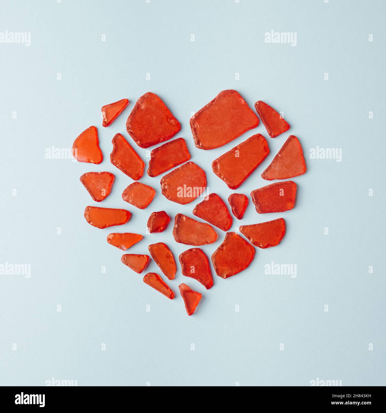 Zerbrochene Glasstücke bilden ein rotes Herz auf einem pastellblauen Hintergrund. Minimales Konzept für Herzschmerz Stockfoto