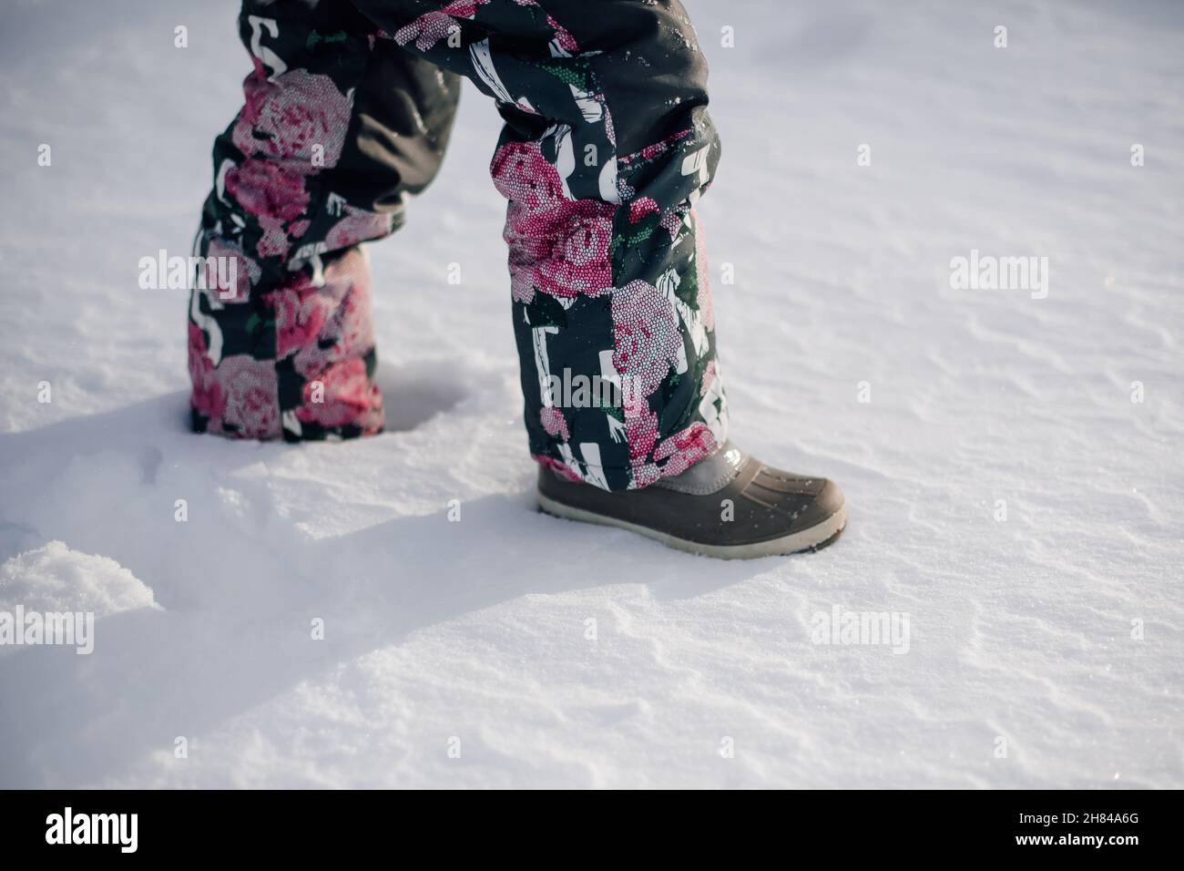 Nahaufnahme von Kinderbeinen im Winteranzug. Seitenansicht der Beine eines kleinen Mädchens, das in Filzstiefeln durch den Schnee läuft, Spaziergang im Winter an frostigen sonnigen Tagen Stockfoto