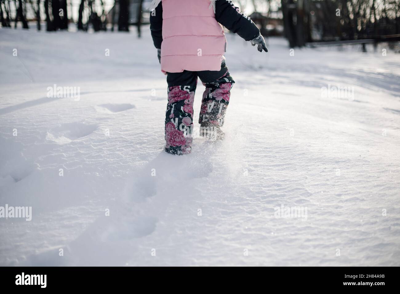 Fußabdrücke von Kinderfüßen im Schnee. Rückansicht eines Kindes in warmer Winterkleidung, das nach einem starken Schneesturm durch Schneeverwehungen spazierengeht und im Wald spielt Stockfoto