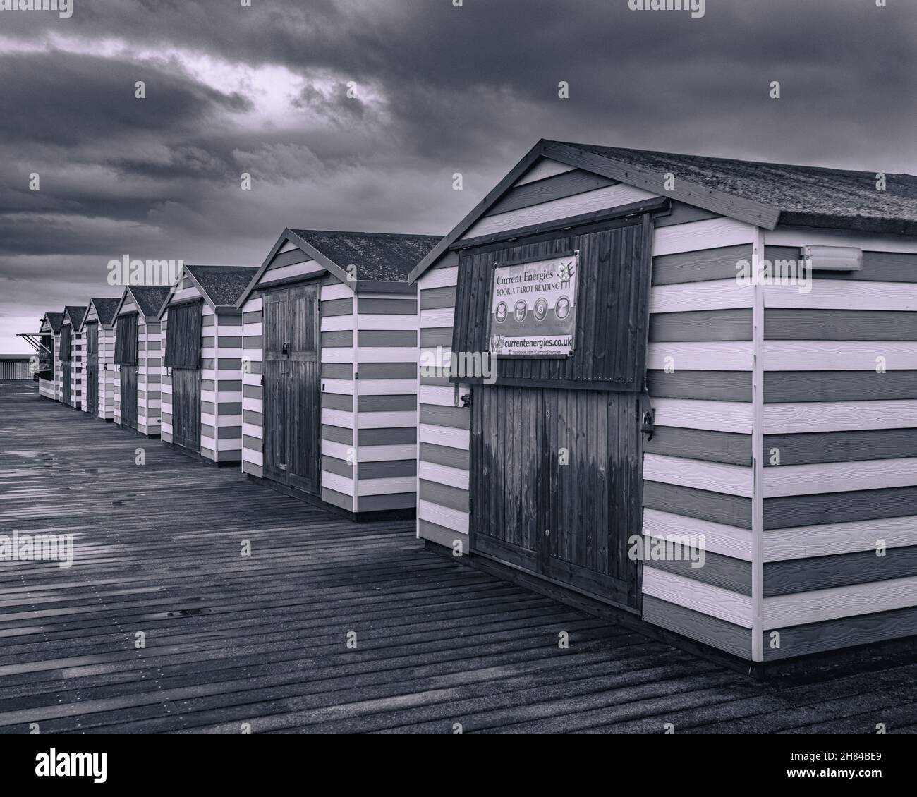 Schwarz-Weiß-Foto von bunten Strandhütten am Hastings Pier, Sussex UK. Düsterer Himmel. Stockfoto