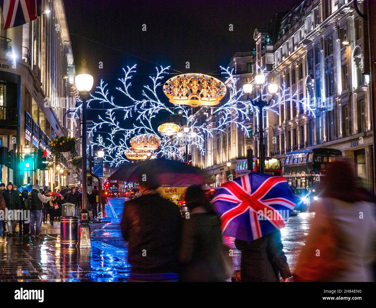 Die Weihnachtseinkäufer DER REGENT STREET und der Regenschirm der Union Jack-Flagge in einem regnerischen Regen fegten die Regent Street mit Weihnachtslichtern hinter der Nacht London UK Stockfoto