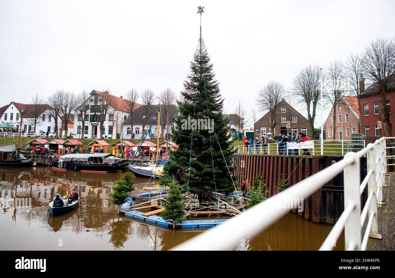 Carolinensiel, Deutschland. 27th. November 2021. Der schwimmende Weihnachtsbaum wird von Freiwilligen im Hafen des Dorfes aufgestellt. Seit 1995 wird der Baum traditionell am Samstag vor dem ersten Adventssonntag aufgesetzt und die Lichter eingeschaltet. Quelle: Hauke-Christian Dittrich/dpa/Alamy Live News Stockfoto