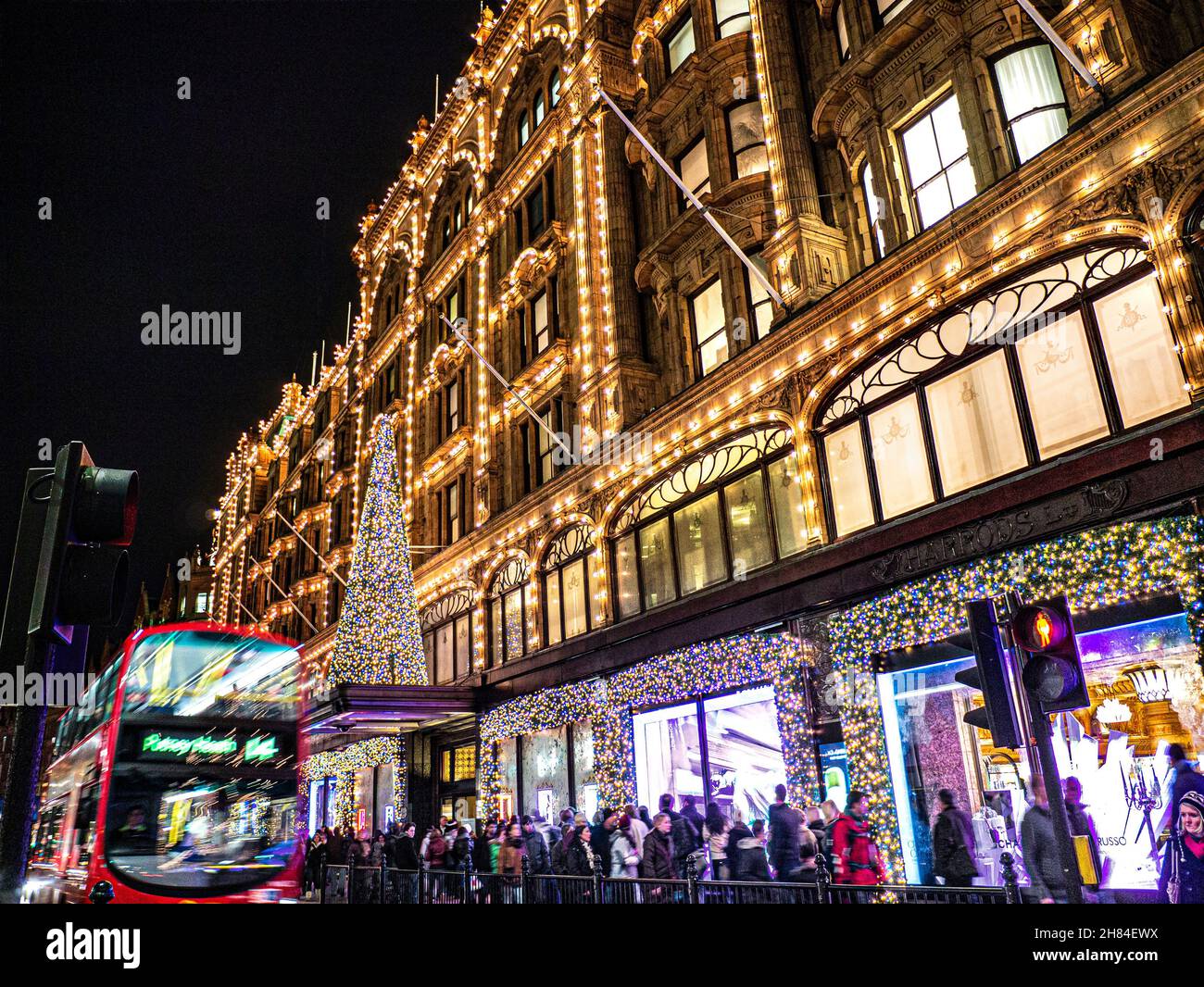 WEIHNACHTEN LONDON SHOPPER LICHTER HARRODS VERWISCHEN DAS GESCHÄFTIGE LONDONER Kaufhaus Harrods in der Abenddämmerung mit Weihnachtslichtern, Einkaufsmassen und dem roten Bus Knightsbridge London SW1 Stockfoto