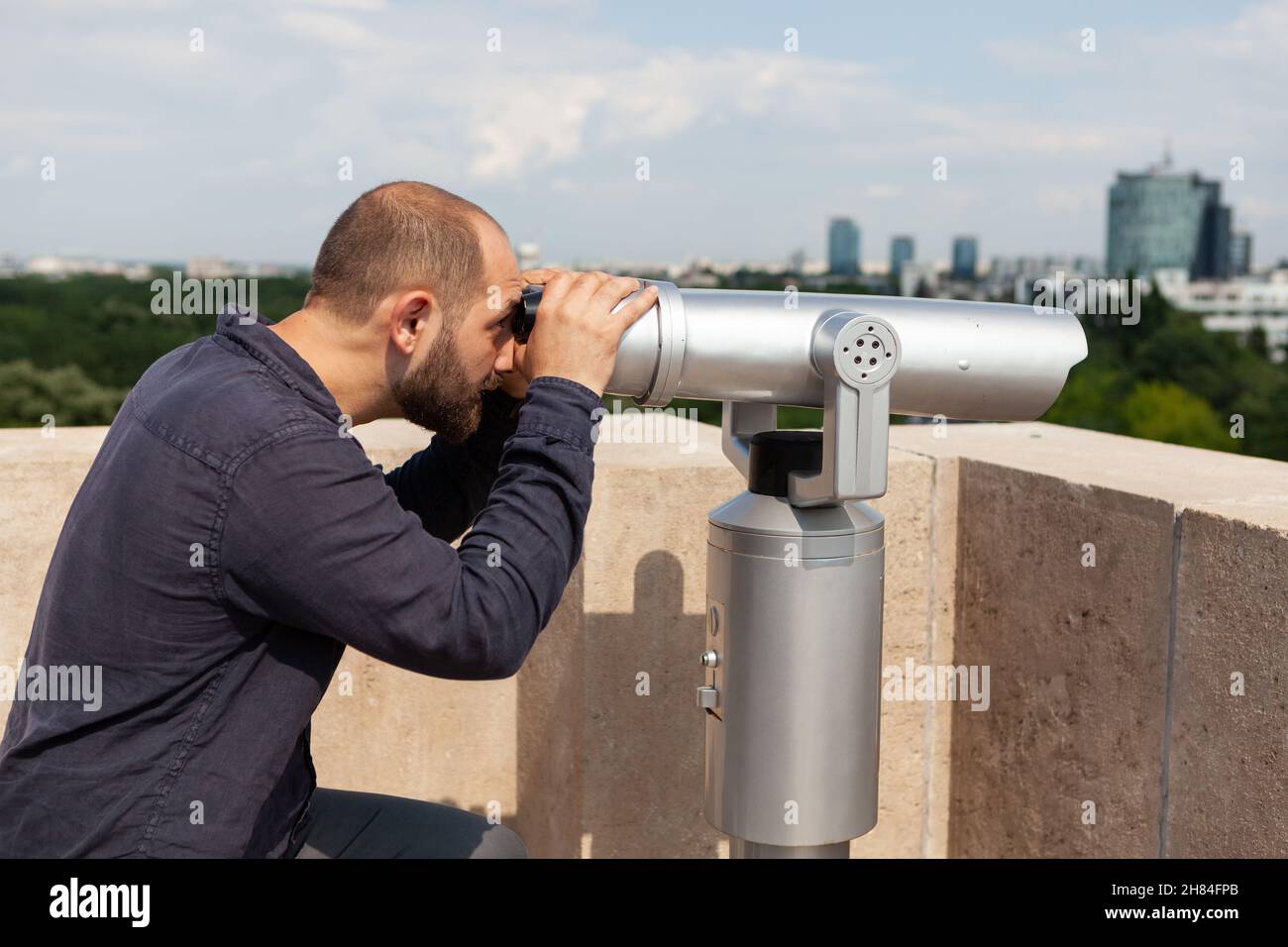 Tourist mit Fernglas-Fernglas Blick auf die städtische Metropole auf dem Turm Gebäude am Beobachtungspunkt stehen. Kaukasischer Mann, der im Sommer Urlaub genießt. Landschaftskonzept Stockfoto