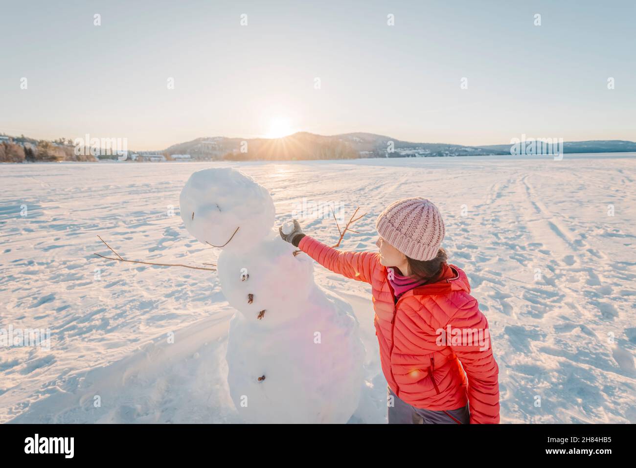 Frau macht Schneemann im Winter See Schnee Natur Landschaft Spaß genießen aktiven Winter Lebensstil bei schönem Sonnenuntergang am sonnigen Wintertag. Stockfoto