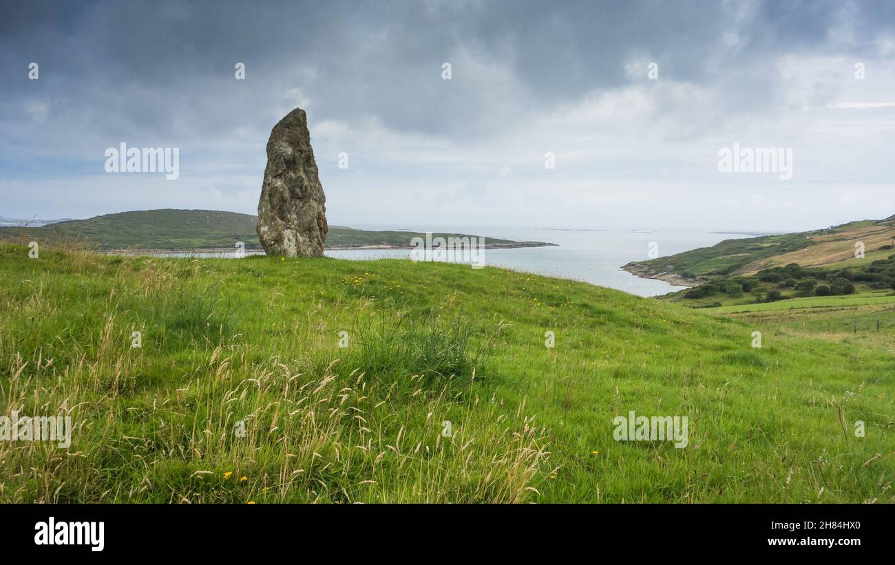 Ein stehender Stein in Clifden, Connemara, Grafschaft Galway im Westen Irlands. Im Hintergrund ist die Mündung der Clifden Bay zu sehen. Stockfoto