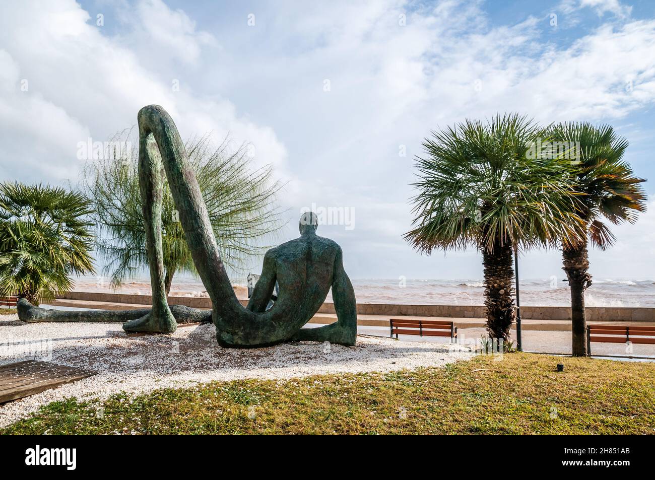 Der Odyssey-Leser, Bronzeskulptur mit der Figur eines sitzenden Mannes, umrissen, mit überproportional langen Gliedmaßen und einem der Beine, die eine Brid bilden Stockfoto