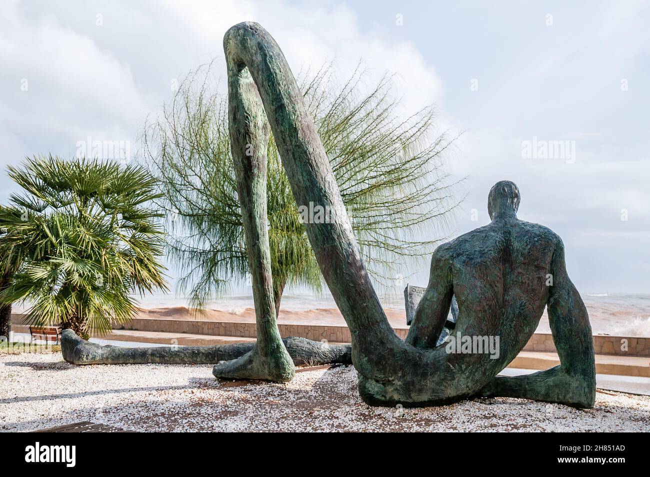 Der Odyssey-Leser, Bronzeskulptur mit der Figur eines sitzenden Mannes, umrissen, mit überproportional langen Gliedmaßen und einem der Beine, die eine Brid bilden Stockfoto