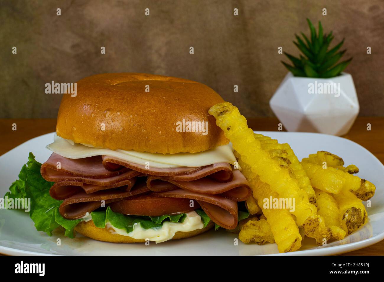 Honigschinken auf einem Brötchen mit Provolone-Käse und serviert mit einer Seite Pommes frites Stockfoto