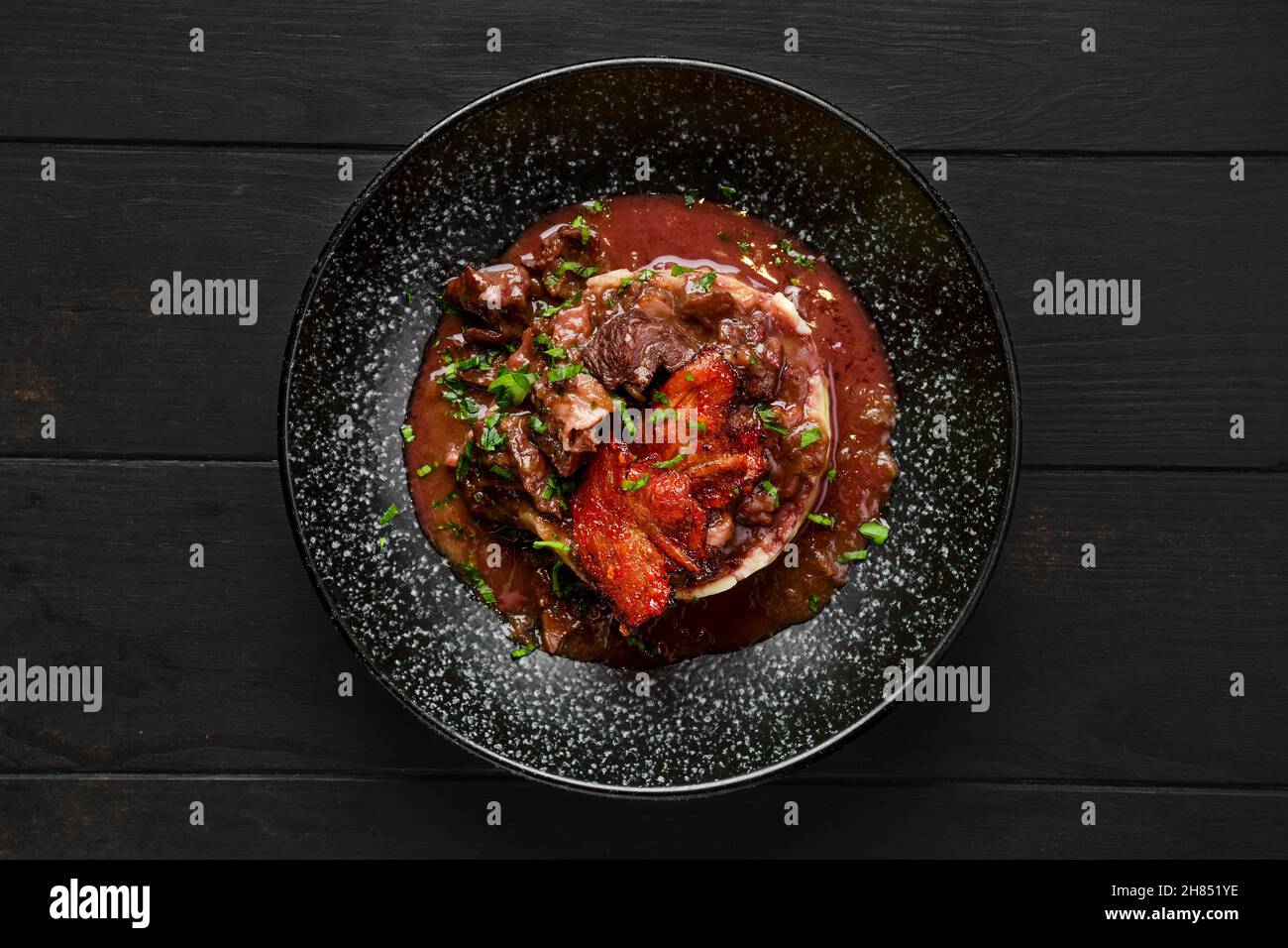 Draufsicht auf Rindergulasch mit Speckchips, Kartoffelpüree und schwarzer Johannisbeersoße auf einem Teller Stockfoto