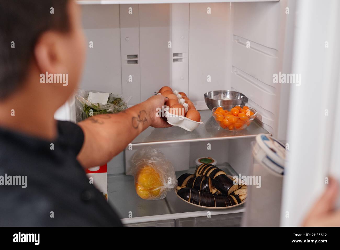 Rückansicht Porträt einer unkenntlichen Frau, die frische Eier aus dem Kühlschrank in der Küche nimmt, Platz zum Kopieren Stockfoto