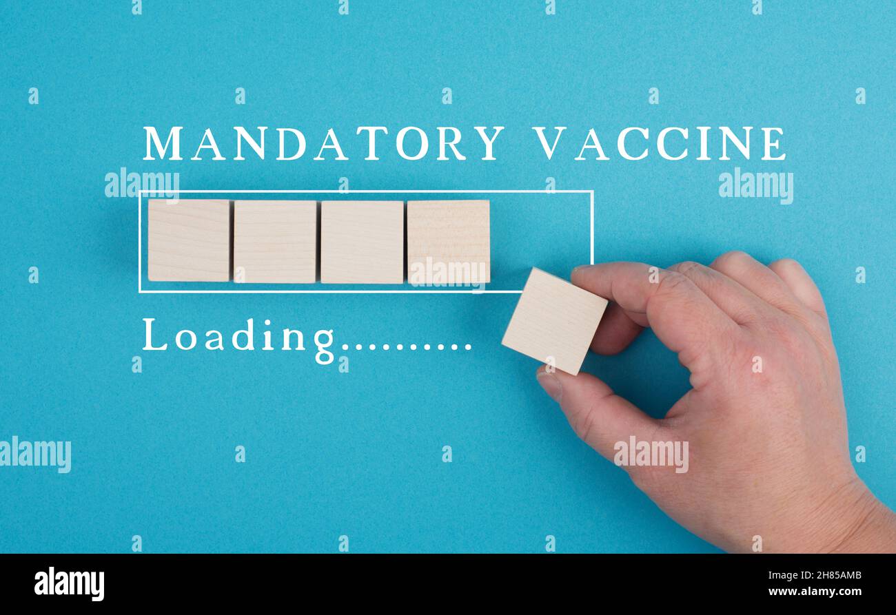 Die obligatorische Impfung steht auf blauem Hintergrund, Ladebalke, Hand legt letzten Würfel Stockfoto