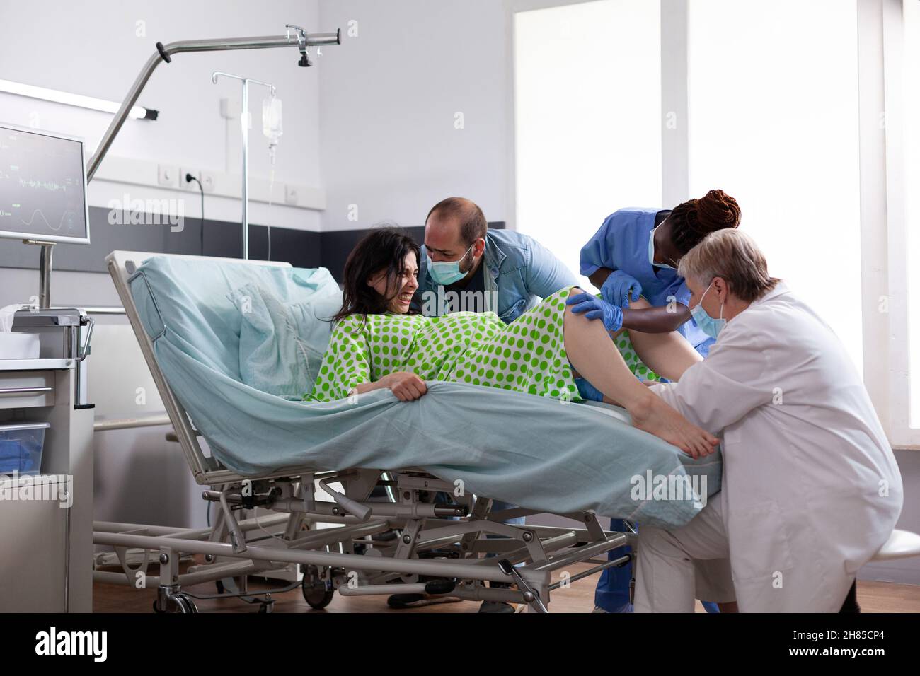 Multiethnisches medizinisches Team, das bei der Entbindung von Kindern auf der Krankenhausstation hilft. Frau gebiert Baby, während sie im Bett mit Wehen Kontraktionen lag. Arzt und schwarze Krankenschwester bei der Geburt Stockfoto