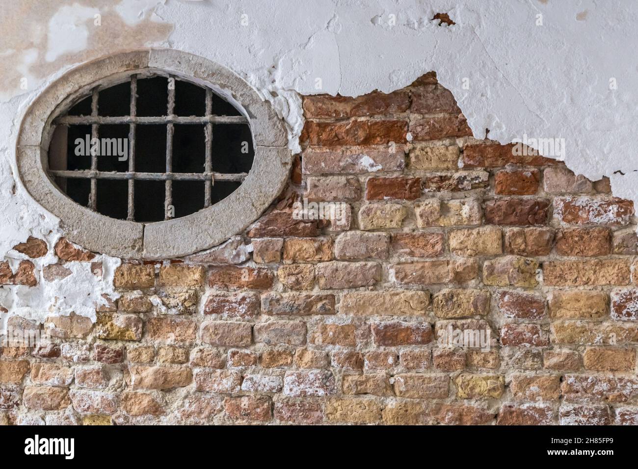 Ziegel- und Stuckwand und ein rundes Fenster, strukturierte Außenwand Stockfoto