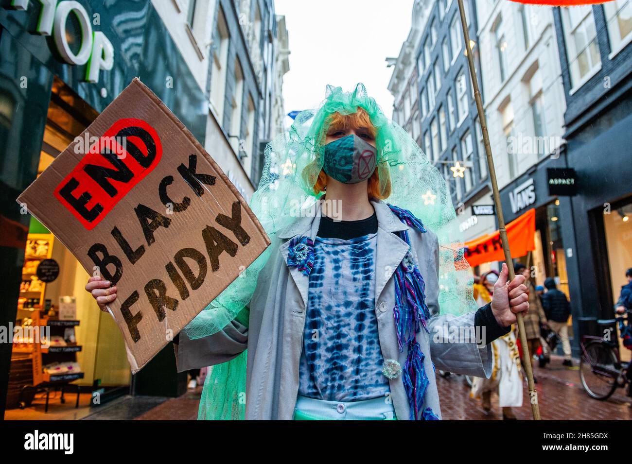 Amsterdam, Niederlande. 27th. November 2021. Ein XR-Aktivist in Second Hand-Kleidung hält während der Demonstration ein Plakat gegen den Schwarzen Freitag.Extinction Rebellion organisierte im Zentrum von Amsterdam eine Modeparade, um die schnelle Mode zu verspotten und die Aufmerksamkeit auf die ausbeuterischen, profitorientierten und grünlichen Praktiken der Fast-Fashion-Branche zu lenken. Die Klimaaktivisten marschierten durch die Haupteinkaufsstraßen, tanzten und trugen reparierte und gebrauchte Kleidung. Kredit: SOPA Images Limited/Alamy Live Nachrichten Stockfoto