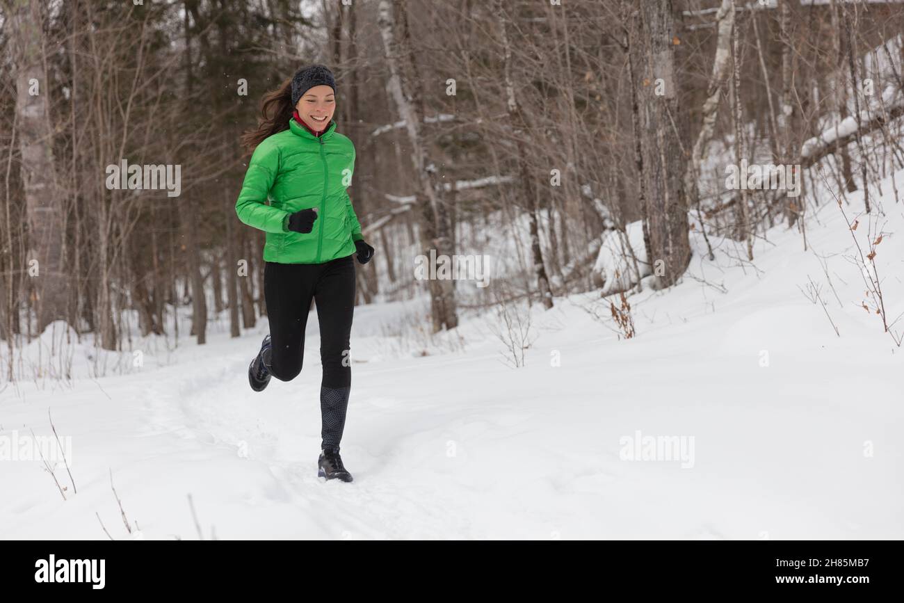 Laufen im Winterschnee. Frau Läuferin joggt draußen an kalten Wintertagen im Wald. Fit gesundes Lifestyle-Konzept mit schönen jungen Fitness-Modell Stockfoto