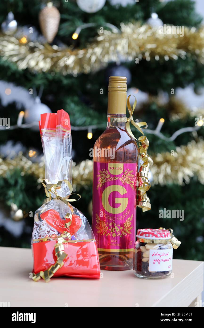 Luomu Rose Glögi - ein traditionelles organisch-alkoholisches finnisches Glogg-Getränk mit Lindt-Schokolade, Rosinen und Mandeln auf einem Tisch mit einem Weihnachtsbaum. Stockfoto