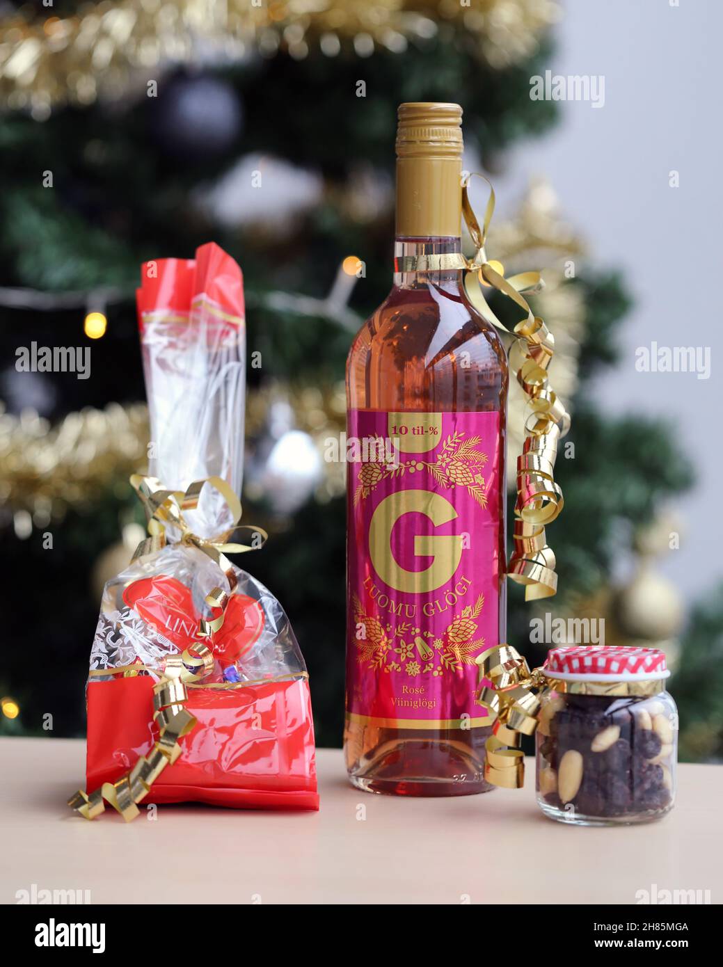 Luomu Rose Glögi - ein traditionelles organisch-alkoholisches finnisches Glogg-Getränk mit Lindt-Schokolade, Rosinen und Mandeln auf einem Tisch mit einem Weihnachtsbaum. Stockfoto