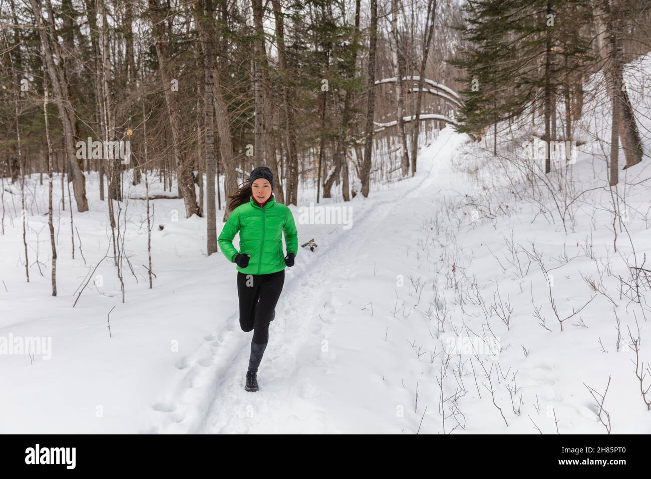 Laufsport Frau. Die Läuferin joggt im kalten Winterwald in warmer, sportlicher Laufkleidung und Handschuhen. Schöne Passform asiatisch kaukasischen Weibchen Stockfoto