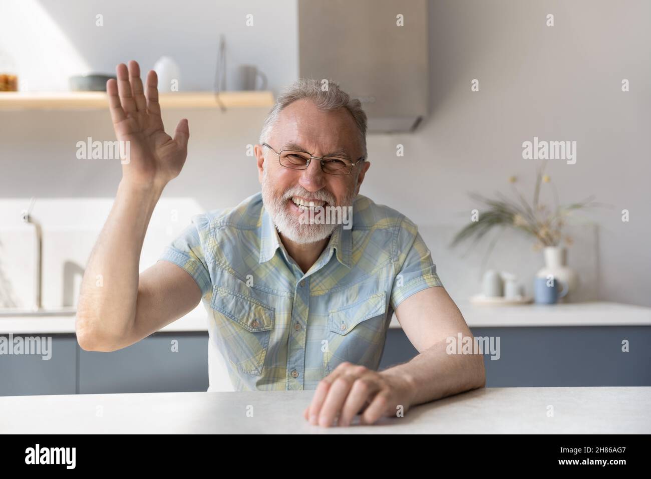 Fröhlicher reifer 60s Mann in Brille winkt Hallo an die Kamera Stockfoto