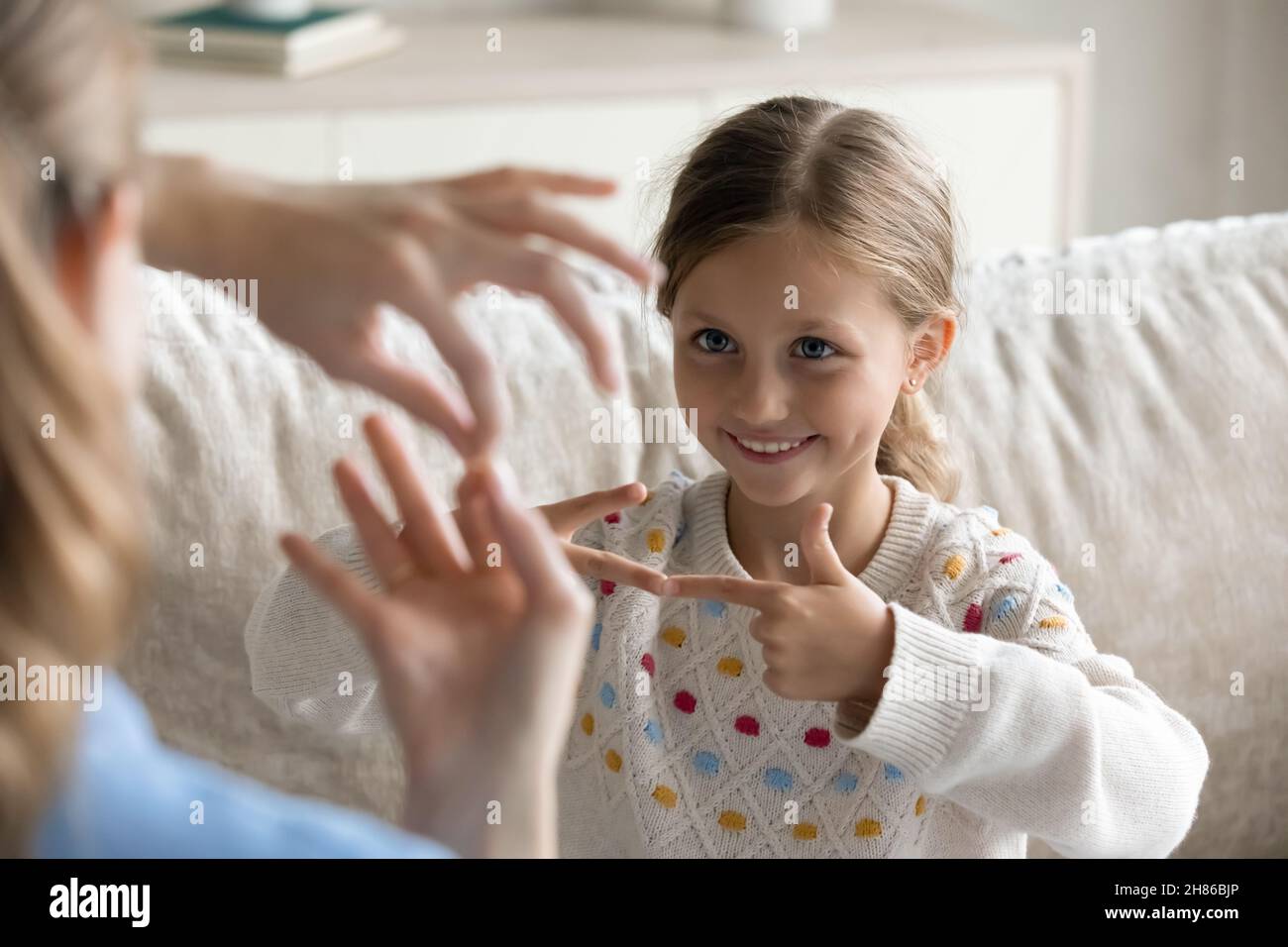 Lächelndes kleines Mädchen, das Zeichensprache mit Mama lernt. Stockfoto