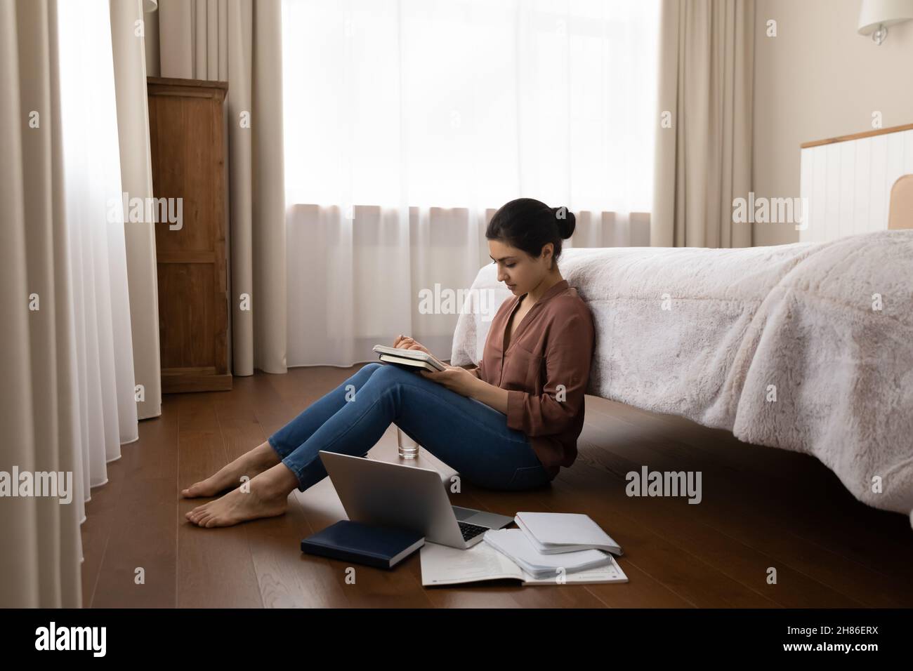 Glückliche junge inderin, die studiert und auf dem Boden sitzt. Stockfoto