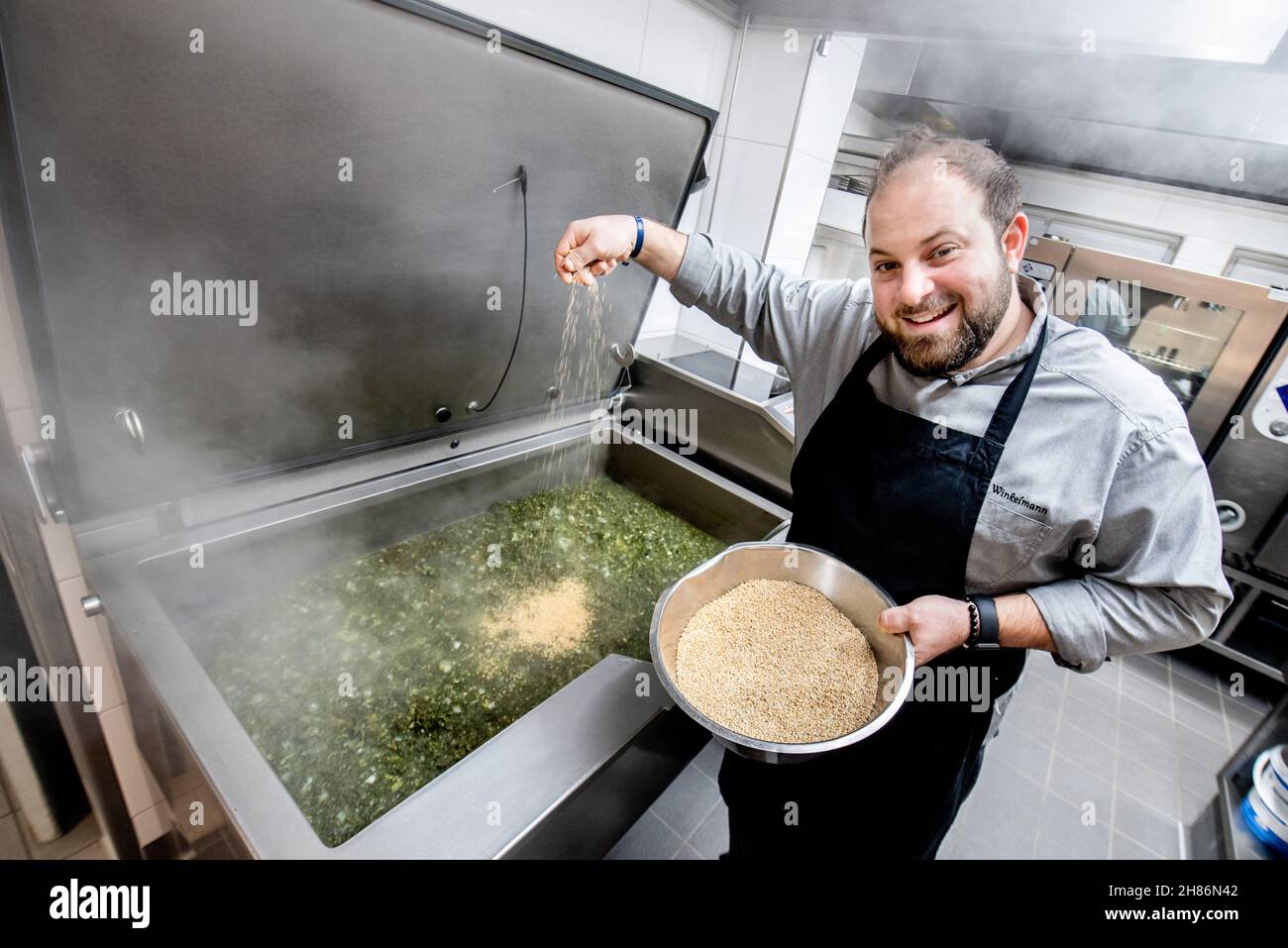 Oldenburg, Deutschland. 18th. November 2021. Nico Winkelmann, Küchenchef und Manager im Bümmersteder Krug, bereitet in der Küche des Restaurants Kohl zu und fügt die Zutat grütze hinzu. Das vitaminreiche Wintergemüse, auch bekannt als Oldenburger Palme, wird traditionell mit Beilagen aus gekochten Kartoffeln, gekochter Wurst, Pinkelwurst und Kasseler serviert. (Zum dpa-Interview 'Wir haben auch Salat aus Grünkohl gemacht') Quelle: Hauke-Christian Dittrich/dpa/Alamy Live News Stockfoto