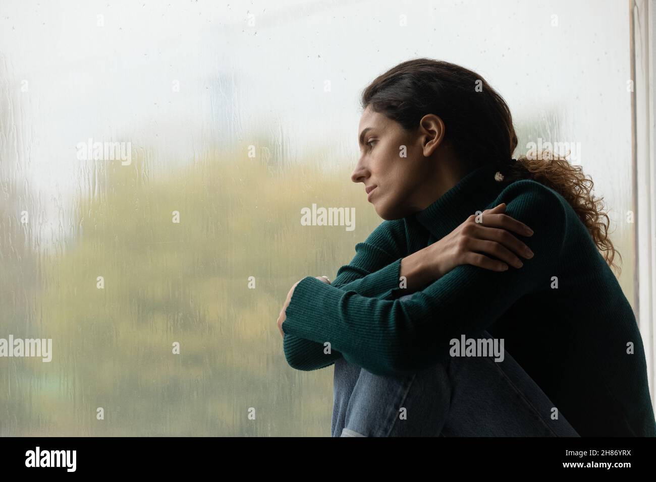 Einsame junge Latina-Hündin sitzt auf dem Fensterbrett und beobachtet draußen den Regen Stockfoto