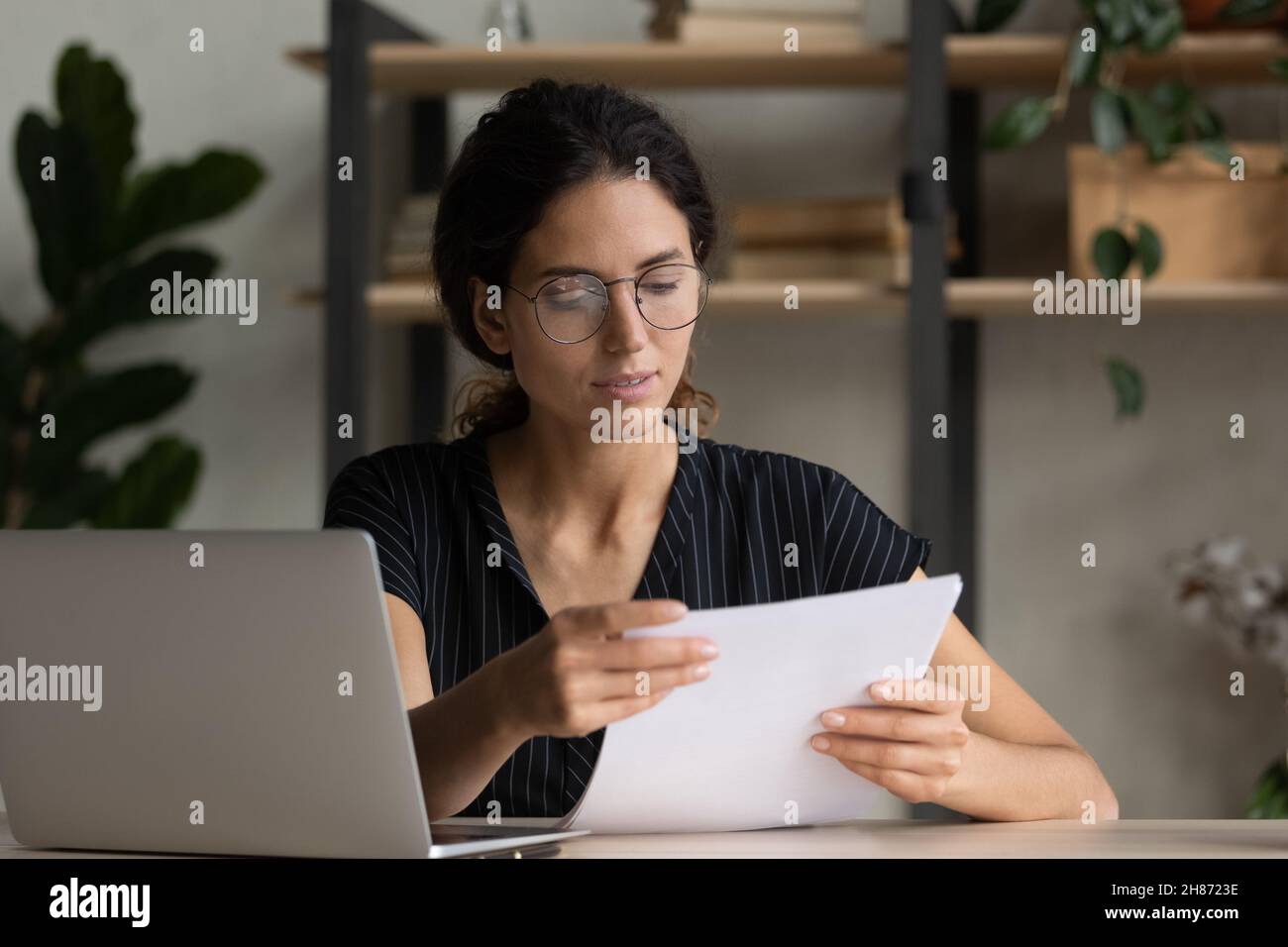 Seriöse junge hispanische Managerin in Brillen studiert Projektdokumentation Stockfoto
