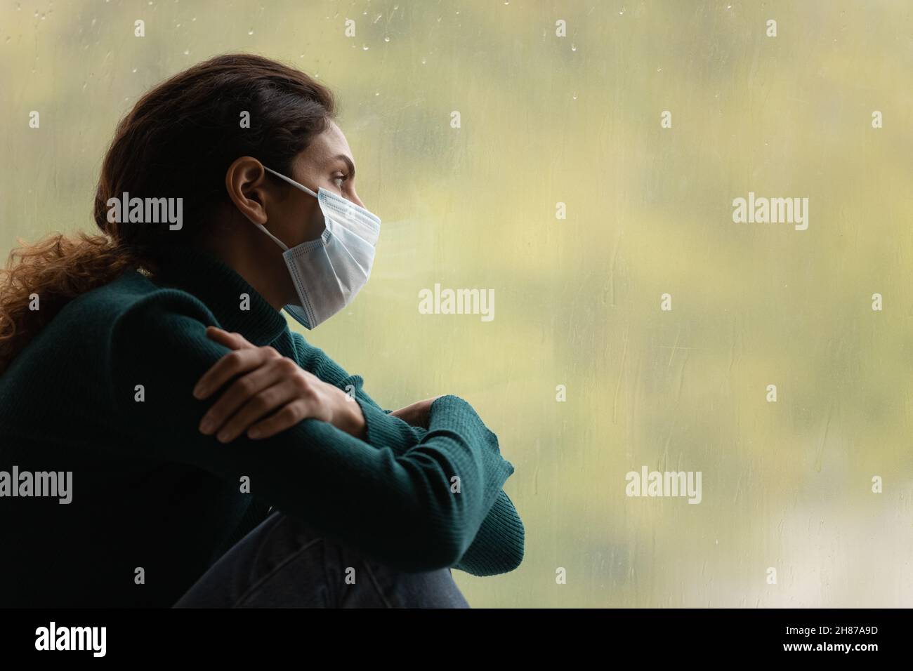 Unglückliche lateinische Frau in medizinischer Maske verbringen Zeit für Fenster Stockfoto