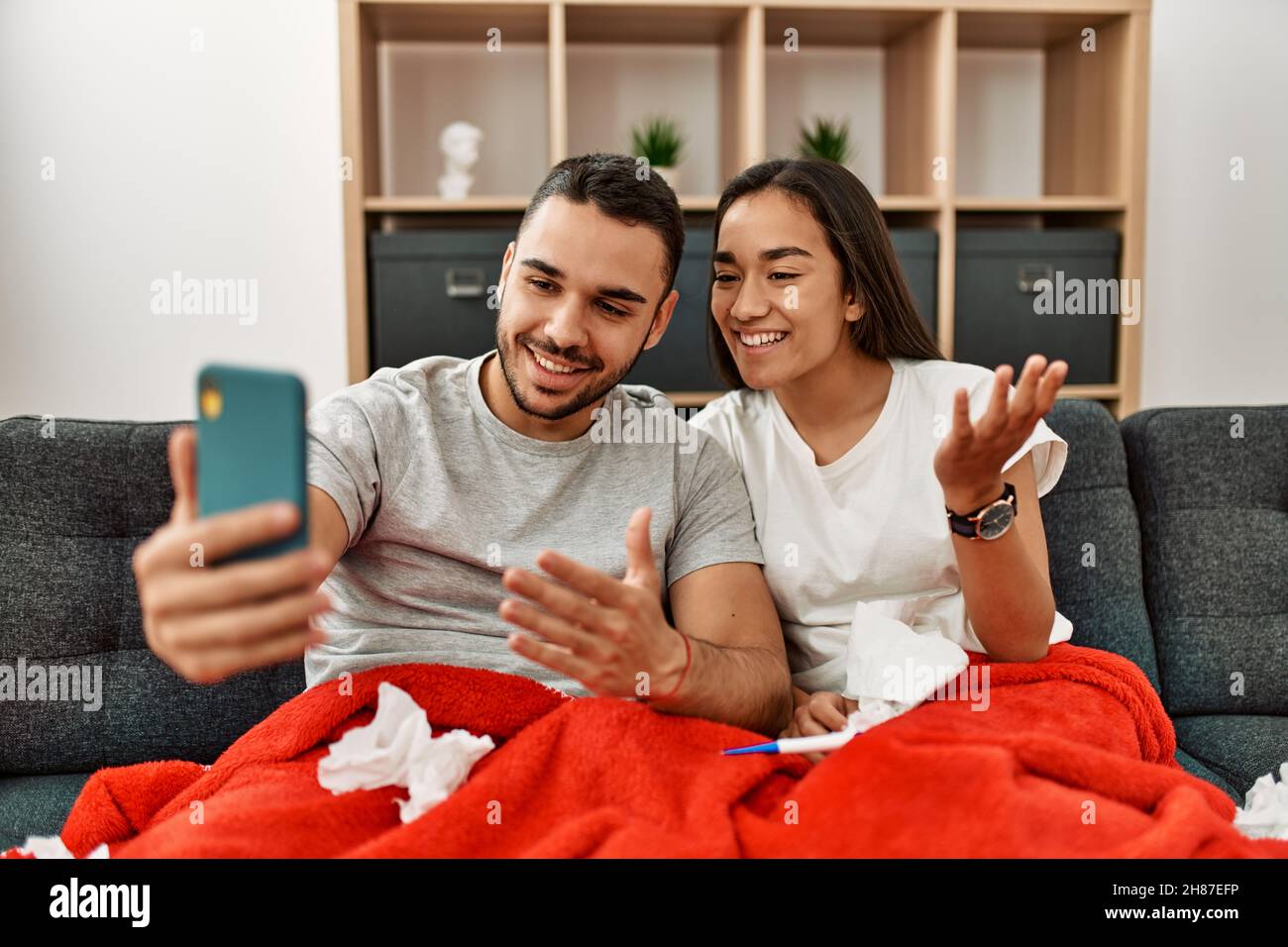 Junges lateinamerikanisches krankes Paar, das zu Hause eine medizinische Fernsultation mit dem Smartphone hat. Stockfoto