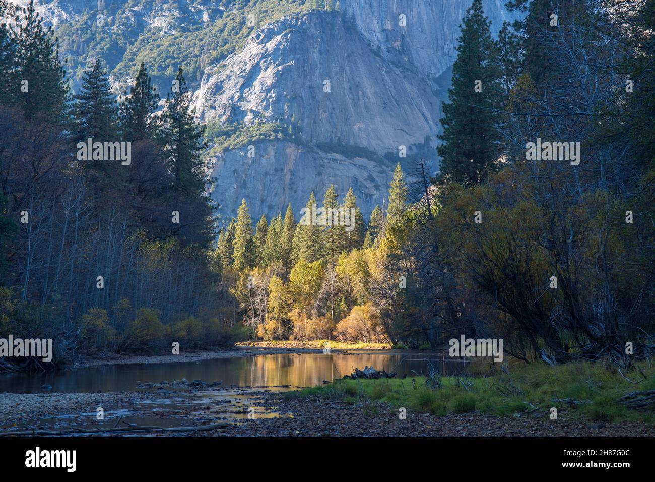 Yosemite-Nationalpark, Kalifornien, USA. Blick auf den ruhigen Merced River in der Nähe von Yosemite Village, herbstliche, hohe Granitklippen, die sich über dem Hotel erheben. Stockfoto