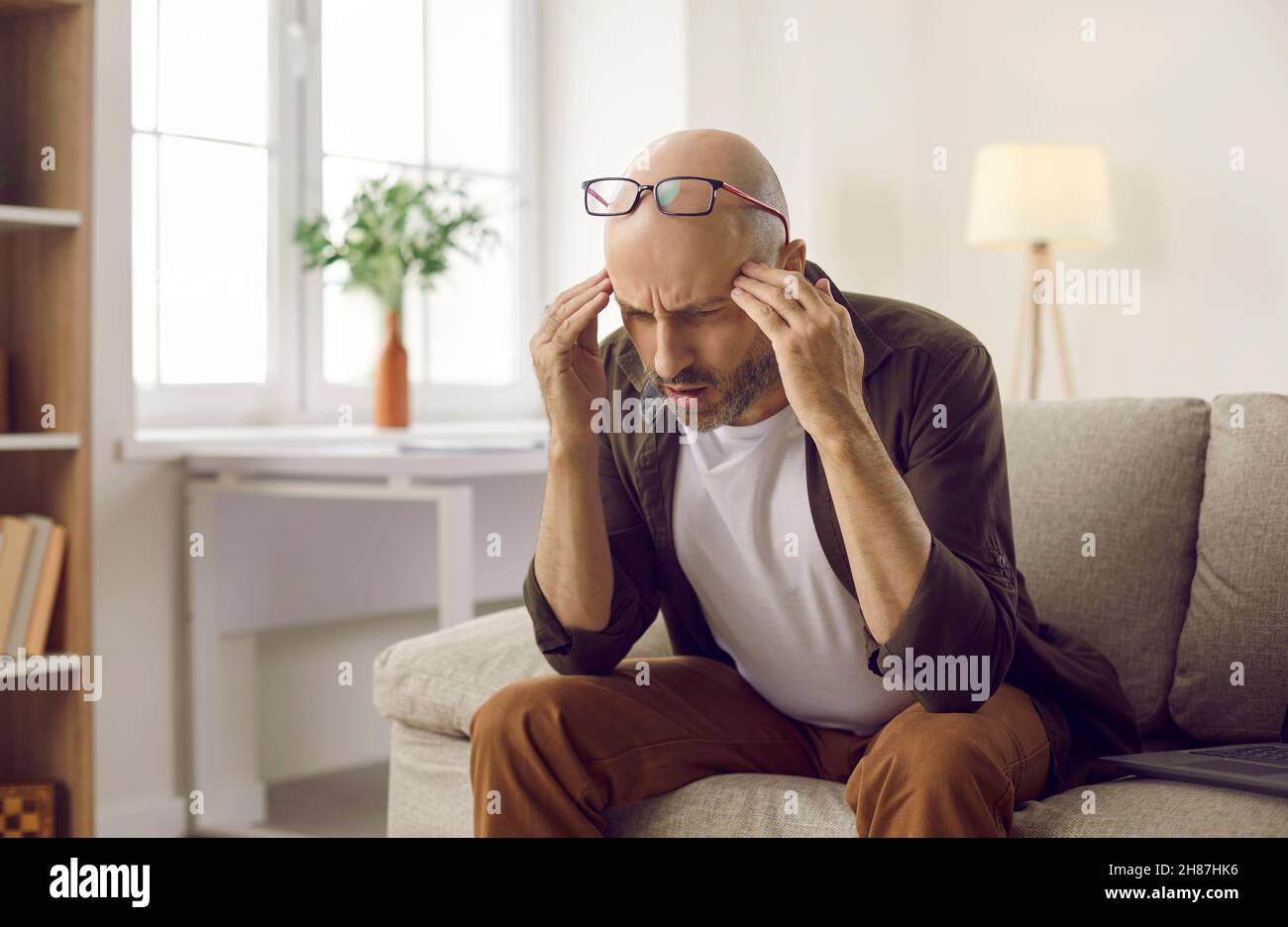 Verwirrt Mann auf der Couch sitzen und denken versuchen, etwas zu verstehen oder sich daran zu erinnern Stockfoto