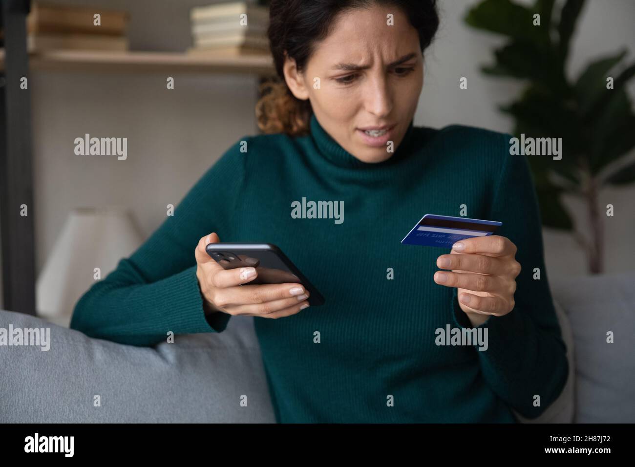 Schockierte junge lateinische Dame, die per Telefon die Bankkarte abgelehnt sah Stockfoto