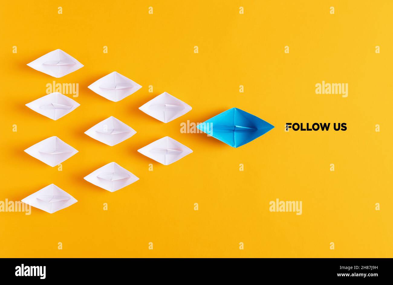 Gelbes Papierboot führt weiße Papierschiffe mit der Follow US-Nachricht. Social-Media- oder Internet-Follower-Konzept. Stockfoto