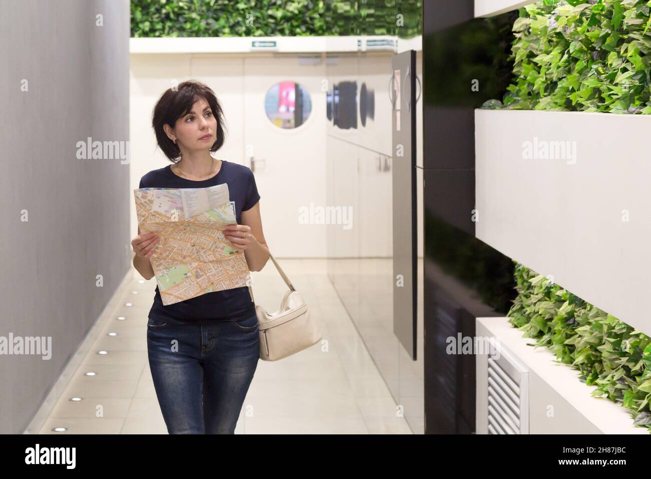 Eine Kundin mit einer Zeichnung in den Händen sucht in einem riesigen Einkaufszentrum nach dem richtigen Laden. Stockfoto